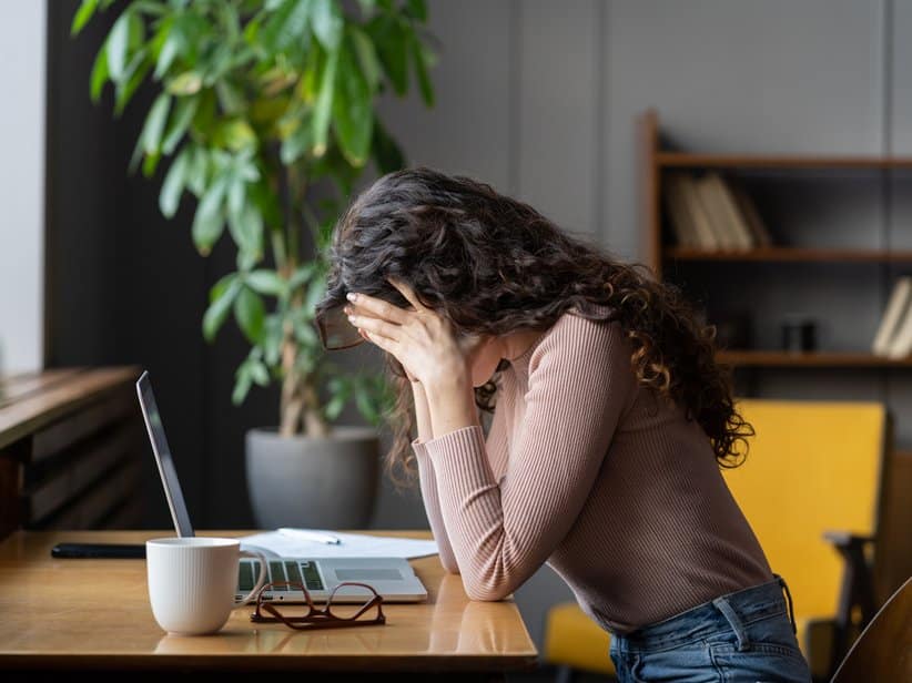 Burnout-Symptome – Person sitzt erschöpft am Schreibtisch, Hände auf der Tastatur