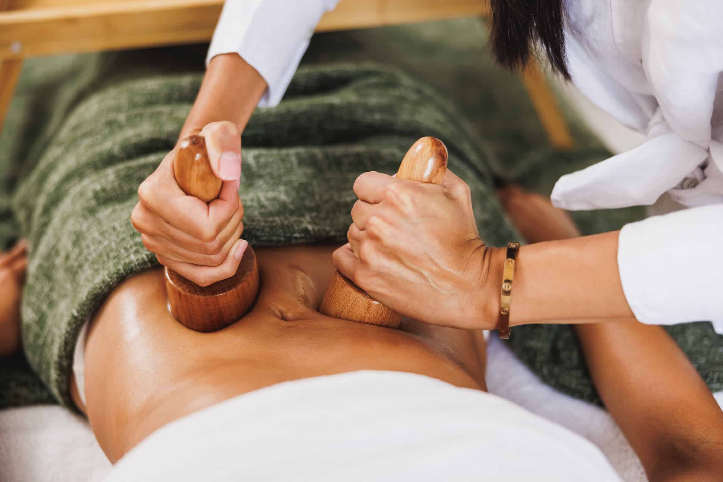 Fachkraft bearbeitet den Bauch mit Holzwerkzeugen bei einer Maderotherapie