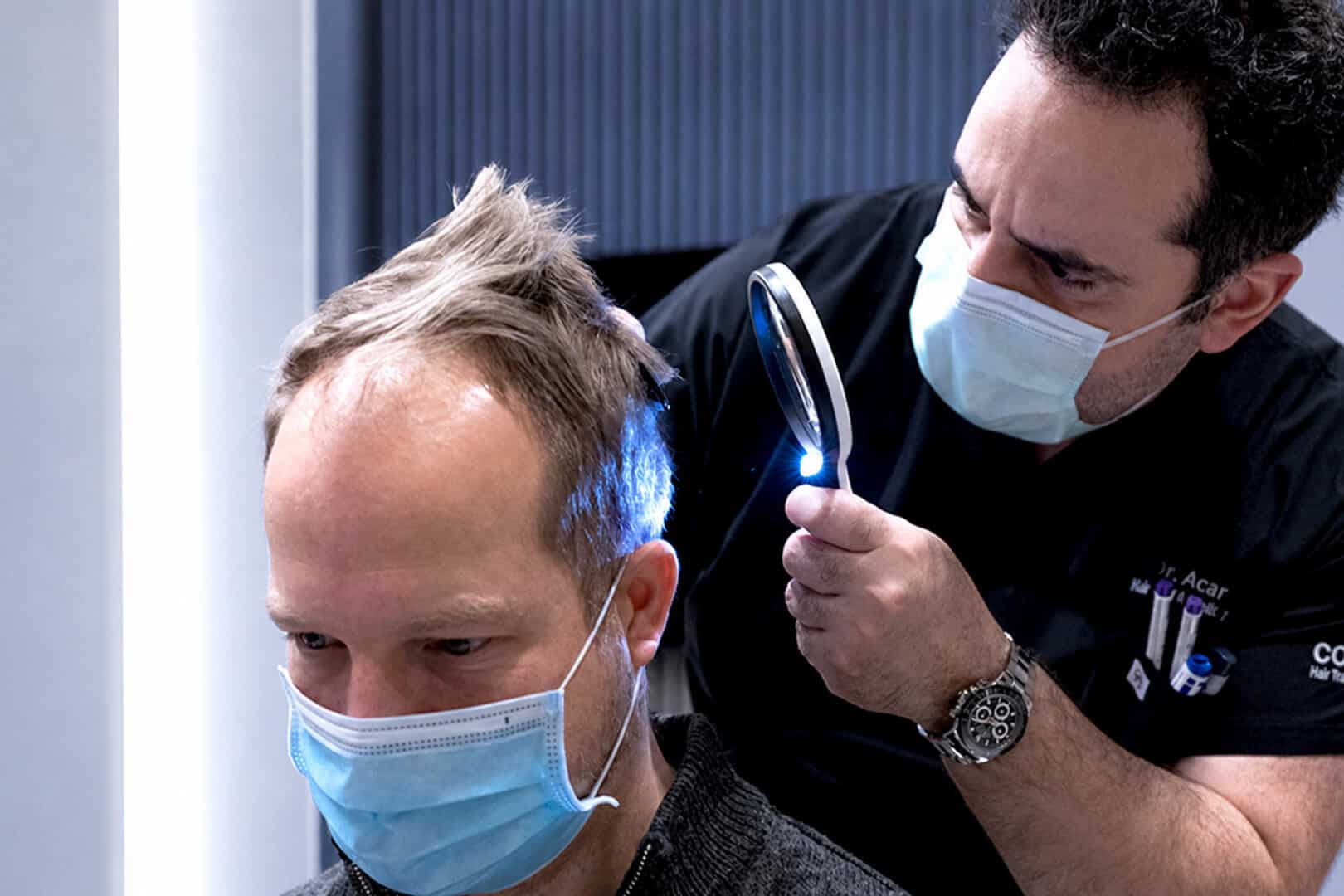 Arzt untersucht die Kopfhaut eines Patienten mit Lupe vor der Haartransplantation