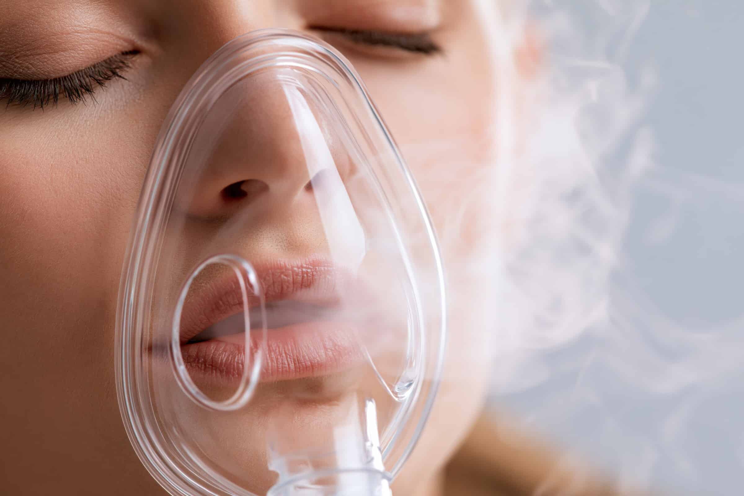 Nahaufnahme einer Frau mit medizinischer Sauerstoffmaske und sichtbarem Atemnebel