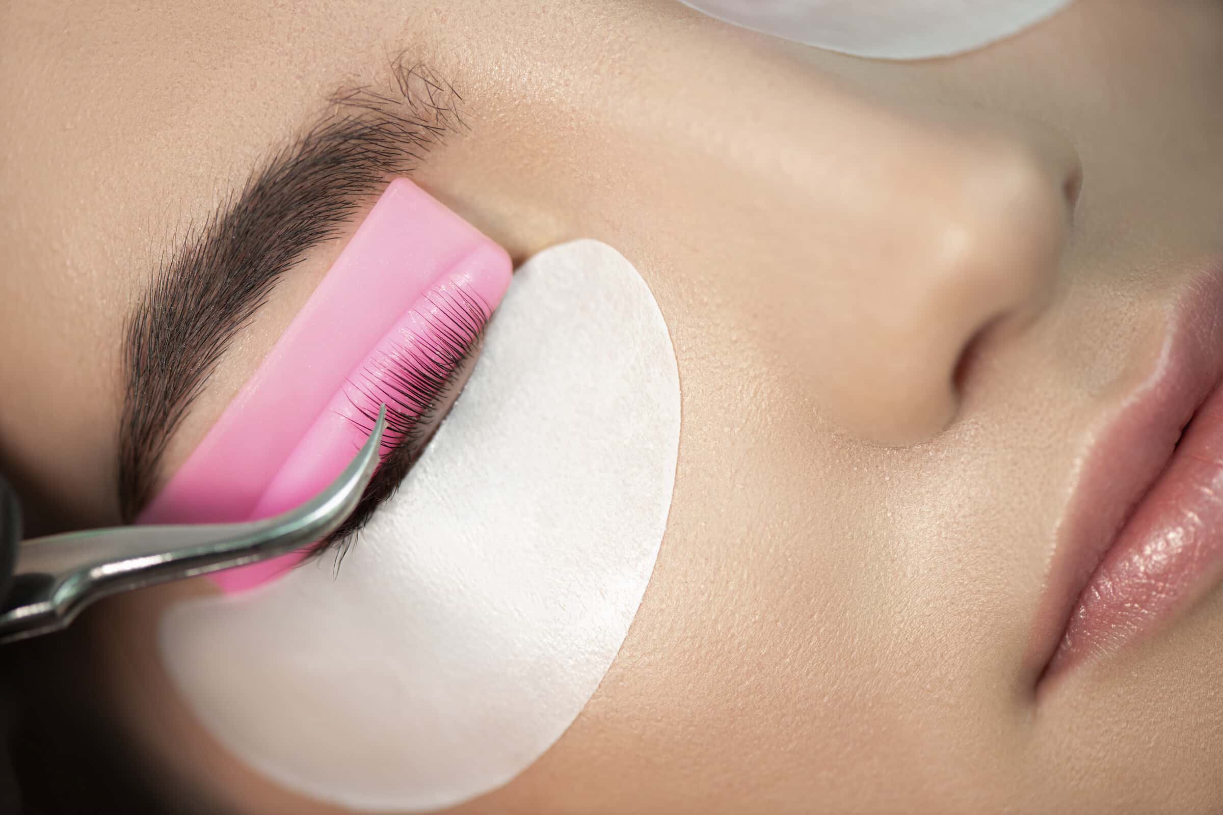Wimpern werden bei der Laminierung mit einer Bürste über das Pad gekämmt