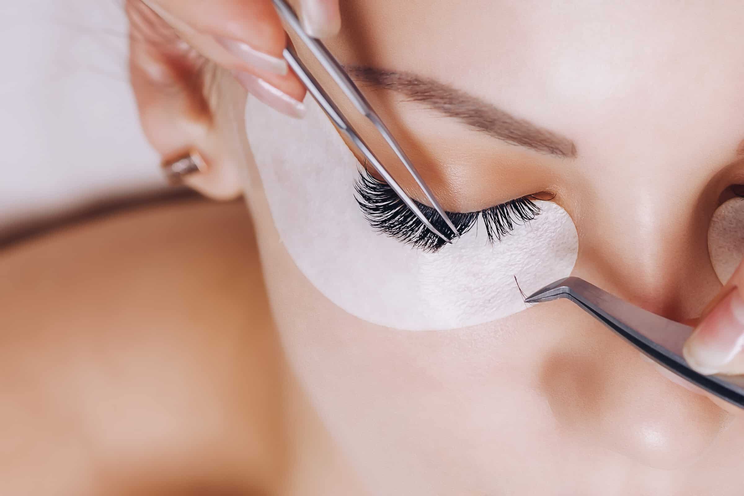 Stylistin arbeitet mit zwei Pinzetten an den Wimpern einer Kundin